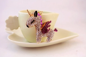 Detailed close-up of a crystal unicorn keychain resting on a white ceramic tea cup set