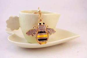 Macro detail of bee keychain with crystal rhinestones and golden enamel on a ceramic cup