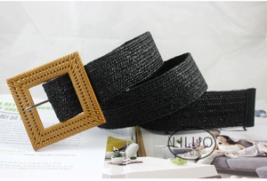 Detail of black woven belt featuring a large square straw-style buckle with a metal pin