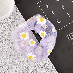 Detail of purple mesh hair scrunchie with white daisy prints on a marble surface