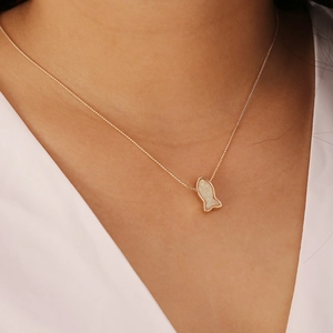Close-up of golden mermaid fish pendant with white opal inlay worn by a model
