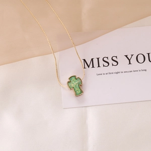 Macro detail of a green cross pendant with gold chain on elegant fabric background