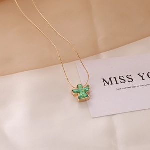 Detail of a gold necklace featuring a green glittery angel pendant on silk fabric