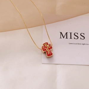 Detailed shot of a gold cross necklace with red glitter pendant on white satin fabric
