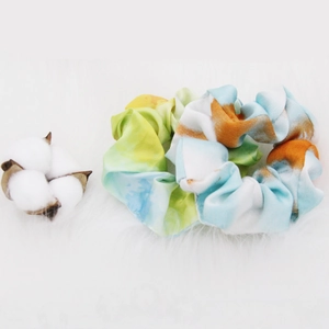 Detail showing two tie-dye gradient fabric scrunchies with soft cotton props on faux fur