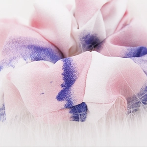 Detail of pink and purple tie-dye fabric scrunchie on white faux fur background