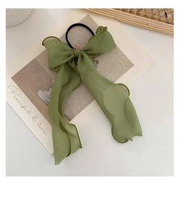 Close-up of a green tulle bow hair scrunchie with dark green piping on a white desk