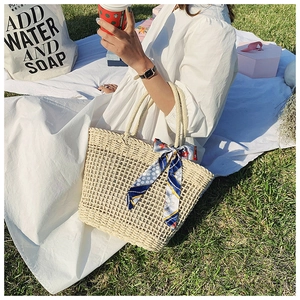 Detail of woven straw tote bag featuring blue printed silk scarf handle in summer setting