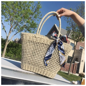 Detail of straw woven tote bag featuring a blue nautical silk scarf and round handles