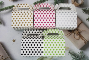 Close-up of five colorful polka dot gift boxes with handles on a festive grey surface