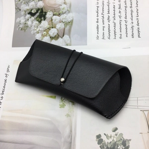 Close-up of black litchi grain leather glasses pouch with elastic strap and metal buckle