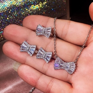 Bow-shaped jewelry set with silver necklace, earrings and ring held against a shiny bag