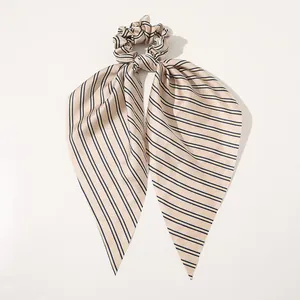 Close-up of elegant silk satin hair scrunchie with navy and gold striped ribbon tails