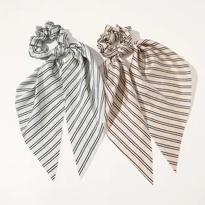 Close-up of smooth satin scrunchies with long ribbons in grey-blue and champagne stripes