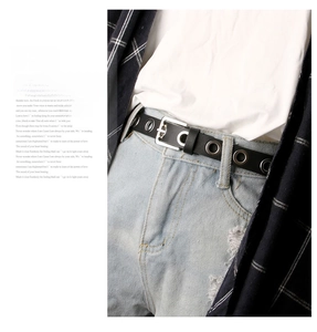 Détail d'une ceinture en cuir noir avec œillets métalliques argentés et boucle carrée