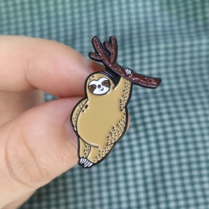 Close-up of a cartoon sloth enamel pin hanging on a branch with detailed metalwork