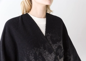 Close-up of black knitted shawl with grey abstract patterns over a white ribbed sweater