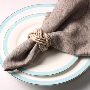 Top view of beige braided rope napkin ring on a grey linen cloth with white ceramic plates