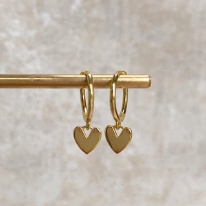 Elegant gold hoop earrings with heart charms hanging on a metal rod for jewelry display