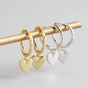 Elegant gold and silver S925 heart charm hoop earrings displayed on a metallic stand