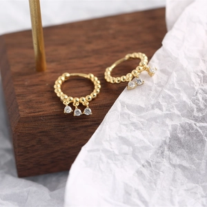 Detail of gold hoop earrings with three zircon tassels on white textured background