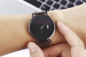 Wrist shot of black YOLAKO quartz watch with date window and mesh strap in office setting