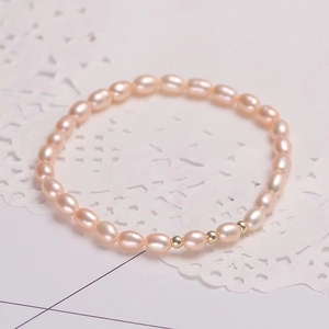 Dettaglio di bracciale di perle rosa ovali con perline dorate su pizzo bianco