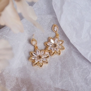Elegant gold flower earrings with micro-set zircon petals on a textured white background