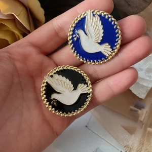 Detail of round enamel brooches with white dove pattern and golden braided texture border