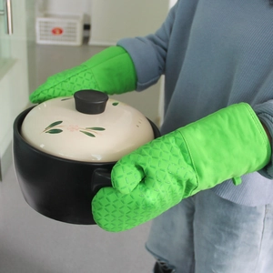 Green silicone oven mitts with diamond texture holding a ceramic pot for heat protection