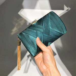 Detail of dark green satin evening clutch featuring pleated texture and golden tassel