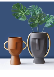Dettaglio di vasi viso in ceramica moderna color caramello e grigio con manici oro