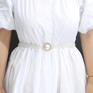 Detail of multi-row white pearl belt with a rhinestone buckle on a white dress