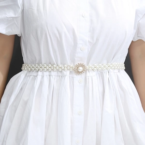 Close-up of elastic white pearl waist belt featuring a sparkling rhinestone flower buckle
