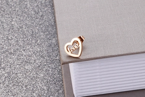 Detail of rose gold heart stud earring with cutout love lettering on a neutral background