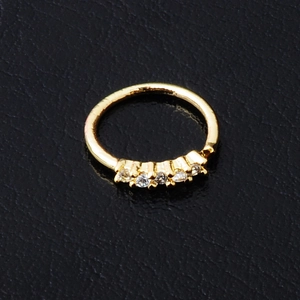 Gold septum hoop ring with five sparkling zircons on a dark textured background