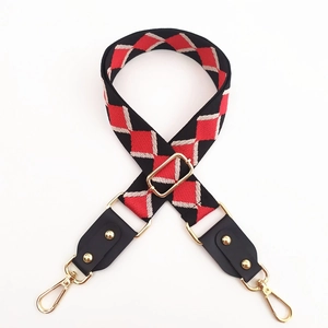 Detail of adjustable woven bag strap featuring red and black diamond pattern and gold hardware