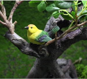 Close-up of a realistic resin bird ornament with yellow and green feathers on a tree branch