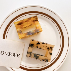 Square tortoiseshell hair claw clip in amber resin finish on white ceramic tray