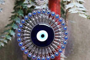 Detailed close-up of large silver metal wall hanging with ornate blue evil eye glass beads