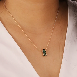 Detail of gold mermaid tail necklace with green stone inlay worn on neck