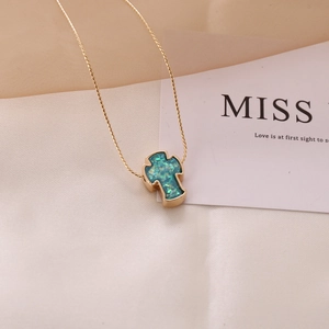 Detailed view of a gold cross necklace with turquoise opal stone on soft fabric