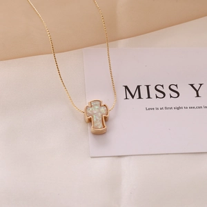 Close-up of golden cross necklace featuring iridescent opal stone on a soft fabric base
