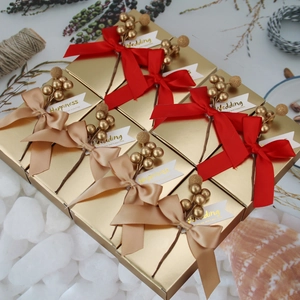 Detailed view of gold wedding gift boxes with red silk bows and festive berry accents