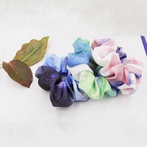 Detail of three colorful fabric hair scrunchies in galaxy gradient patterns on a white base