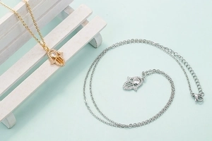 Gold and silver Hamsa hand necklaces with micro-pave cubic zirconia on mint background