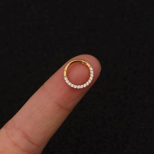 Close-up of a small gold-colored hinged hoop earring with tiny zircons held on a fingertip