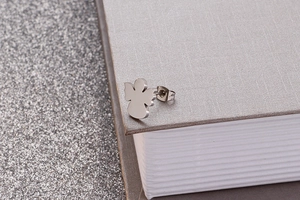 Detailed close-up of a silver angel-shaped stainless steel stud earring on a book edge