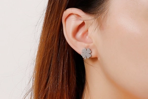 Close-up of a silver four-leaf clover stud earring with a central diamond on a model