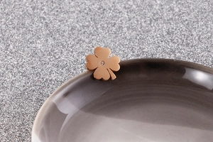 Macro shot of gold four-leaf clover stud earring with central zircon on grey ceramic